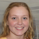 A person with shoulder-length blond hair and a light-colored top smiles at the camera. The background features a neutral setting.