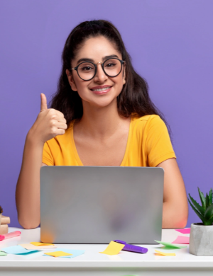 Person in a yellow shirt gives a thumbs-up while sitting at a desk with a laptop, colorful sticky notes, and a small plant against a purple background.