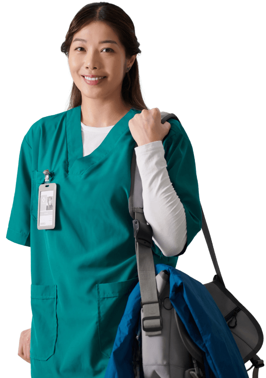 Woman in green scrubs with a name badge smiles while holding a shoulder bag and a blue jacket.